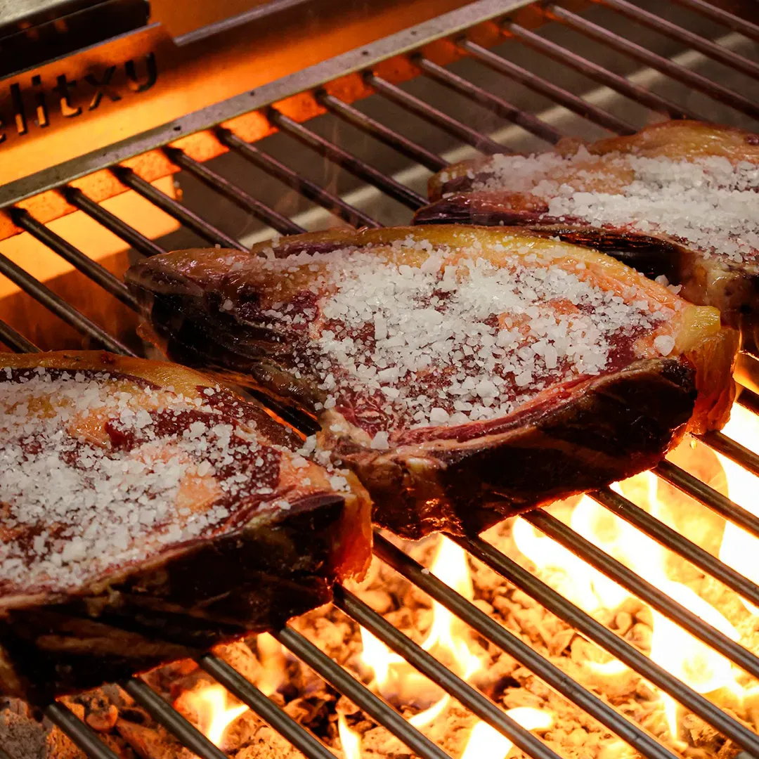 Chuletón sobre una parrilla para asador con brasas de carbón